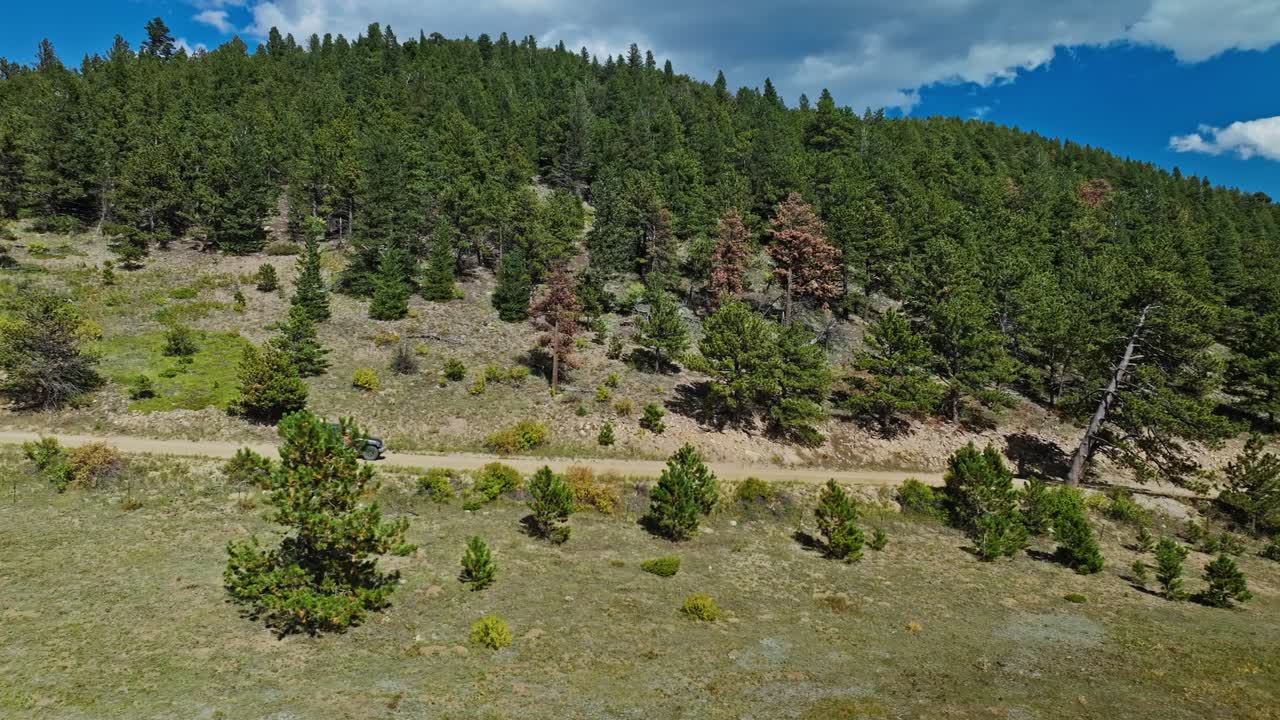 Aerial view of an off-road vehicle driving through a remote forest trail in Boulder, surrounded by dense trees