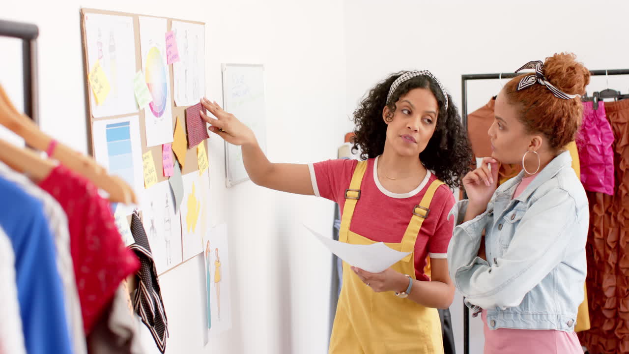 mujeres diseñadoras de moda felices y diversas discutiendo diseños de ropa en el estudio, en cámara lenta