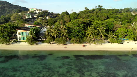 vuelo lateral de un dron mirando una playa en tailandia con casas y un hotel en el fondo