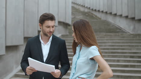 confident businesswoman and businessman working with documents on urban street