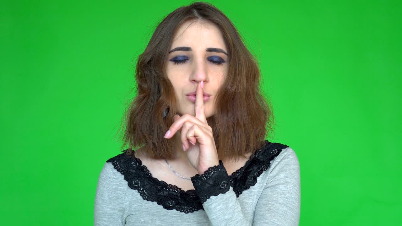 Silence, please! Portrait of young woman holding her forefinger on lips showing hush silence sign