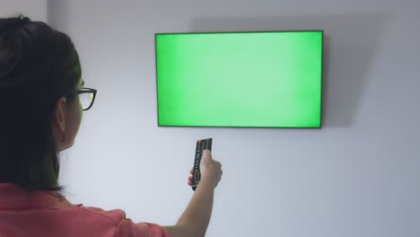 chica con gafas se sienta en un sofá frente a la tv y cambia de canal con un control remoto, llave de croma, primer plano