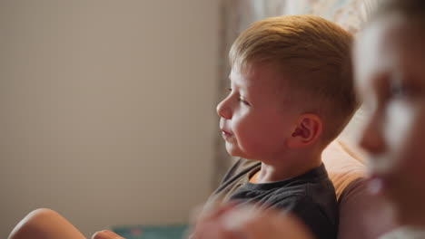 close up of smiling little boy sitting on bed playing and eating berry while blurred image of young girl child appears in foreground creating playful cozy indoor moment filled with laughter