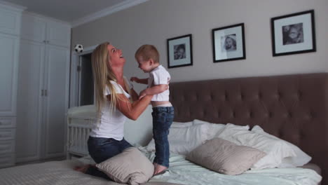 mamá y hijo están jugando en la cama en un dormitorio luminoso, un niño de dos años ríe y sonríe