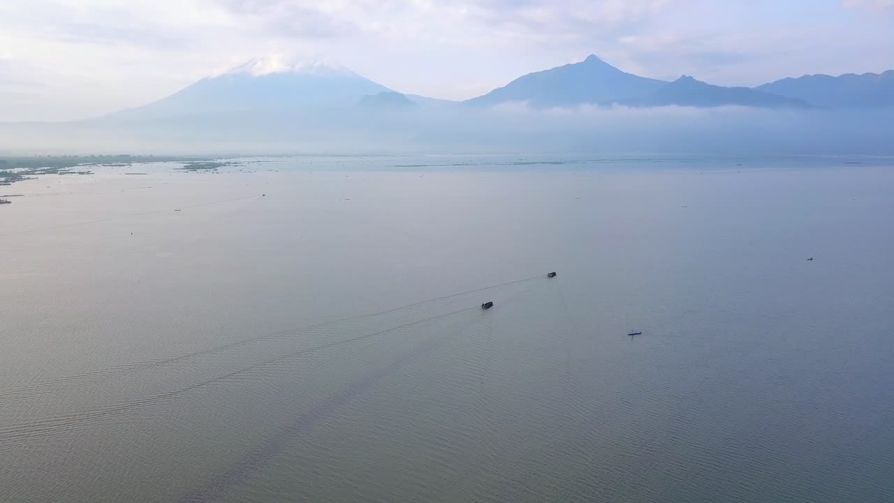 toma panorámica de barcos en el mar con gigantescas montañas detrás de las nubes en el fondo - asia, indonesia