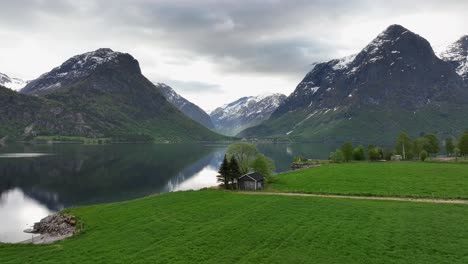 Fascinante-Paisaje-Montañoso-En-El-Parque-Nacional-Jostedal-Con-Campos-Verdes-En-Primer-Plano-Y-El-Lago-Glacial-Oppstrynsvatnet-En-El-Medio---Antena-En-Movimiento-Hacia-El-Valle-Hjelledalen-Durante-La-Primavera