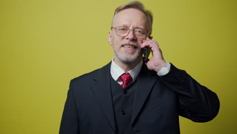 portrait of smiling old businessman talking the cell phone. cheerful mature man in costume talking on the mobile phone on yellow background.