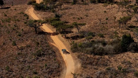 SUV-Vehicle-driving-on-a-dry-dirt-road,-winters-landscape-in-South-Africa,-capturing-serene-views-of-dry-vegetation-and-dust-trail-in-slow-motion