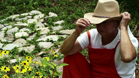 Eine-Erwachsene-Bäuerin-Streichelte-Ihr-Haar-Und-Setzte-Einen-Hut-Auf,-Während-Sie-Vor-Schwarzäugigen-Susan-Wildblumen-Im-Garten-In-Centerville,-Ohio,-USA,-Saß-Und-Lächelte