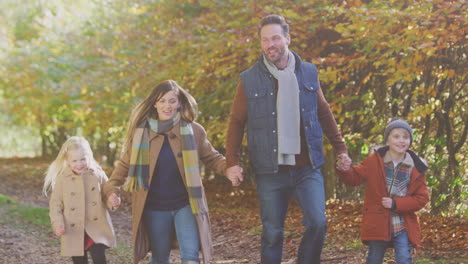 family with mature parents and two children holding hands walking along track in autumn countryside