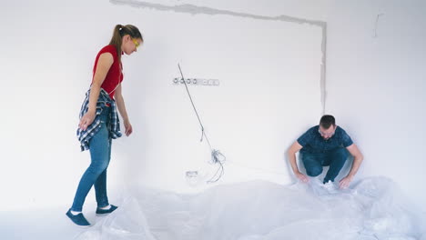 couple covers floor with foil near white wall in own house