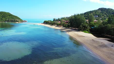 Calm-clear-water-of-lagoon-with-beautiful-patterns-of-corals-and-algae-near-sandy-beach-on-tropical-island-with-lush-vegetation