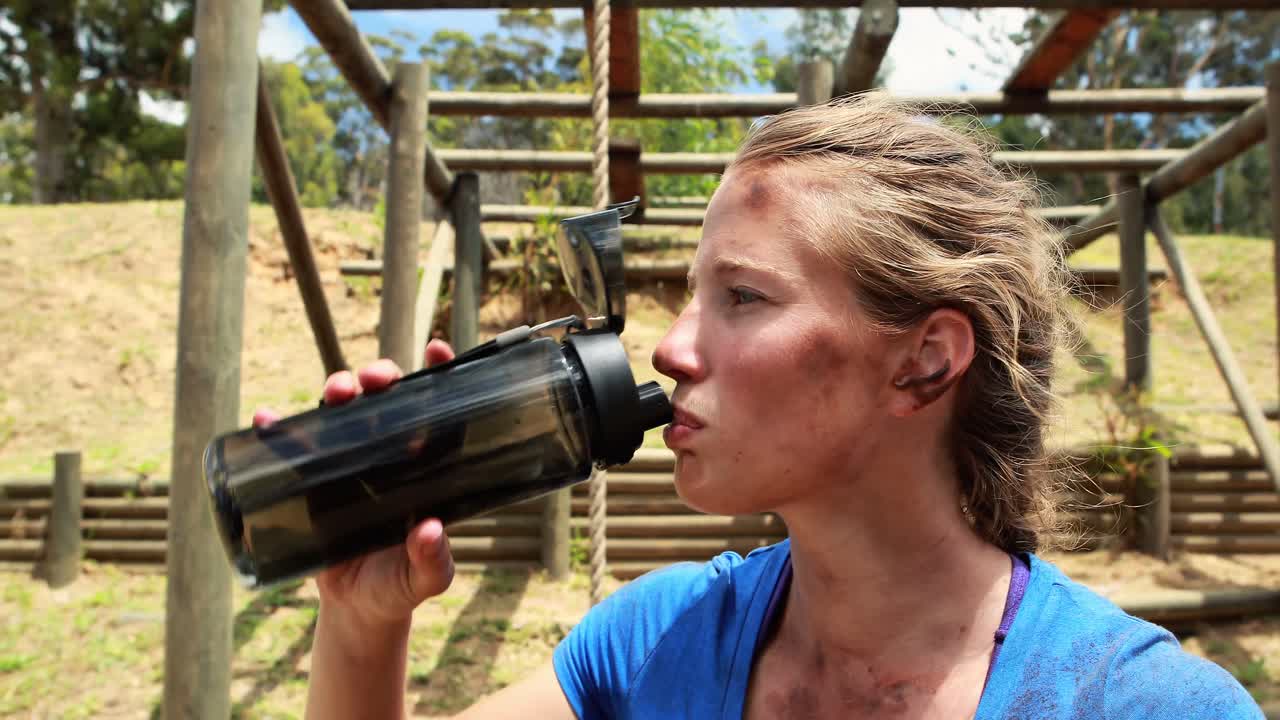 mujer en forma bebiendo agua después del entrenamiento durante una carrera de obstáculos