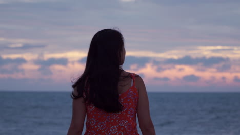 back view of a woman admiring a spectacular sunset with cloudy dramatic sky and colorful reflections on the ocean