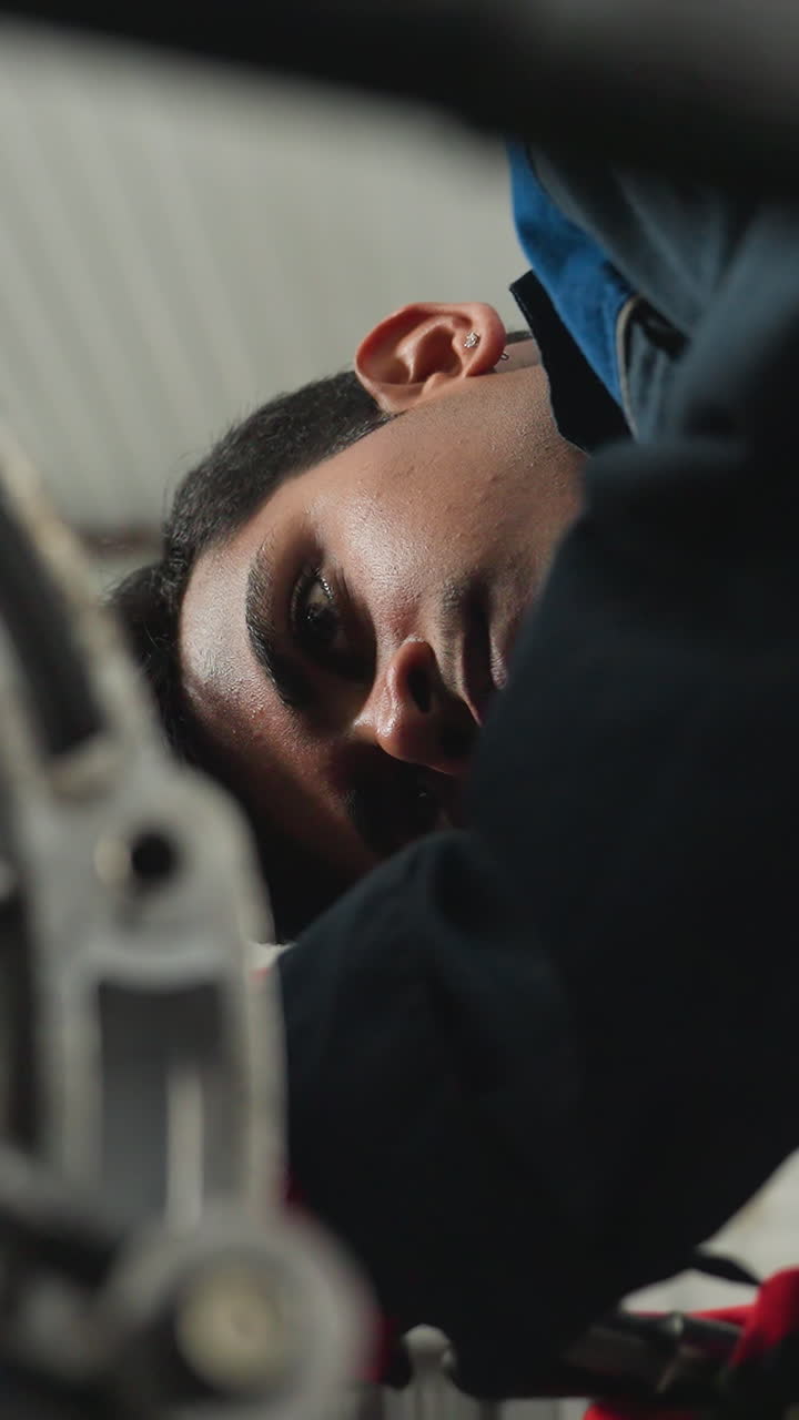 Vista dal basso di un meccanico in uniforme blu che lavora sul motore con un guanto rosso, concentrato su riparazioni e ispezioni dettagliate in un'officina automobilistica.