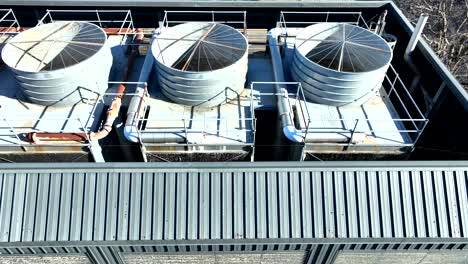 drone view moving to the left of an industrial hvac system with cylindrical towers and metal pipes on a rooftop under bright sunlight