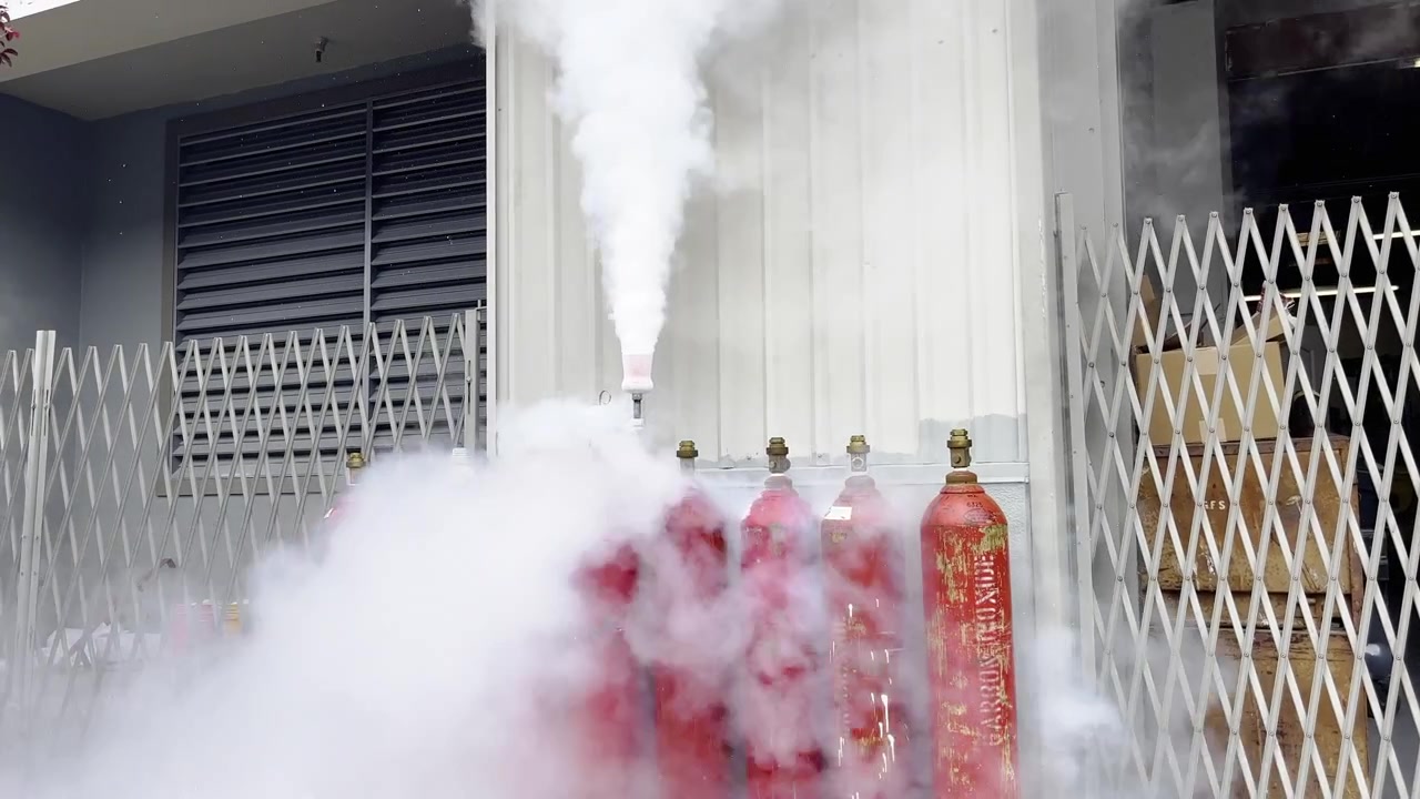 Static view shows expired fire extinguishers releasing dense white gas outdoors