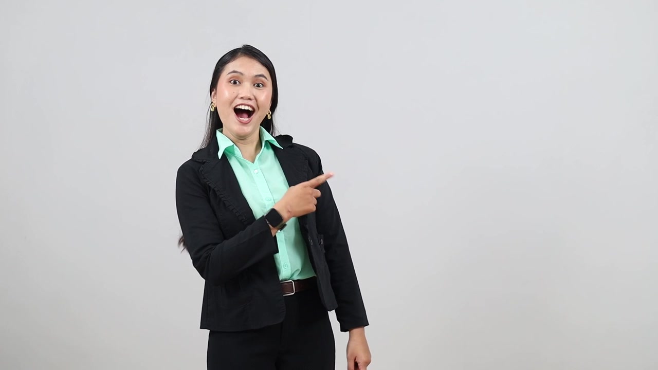 Affermata donna d'affari asiatica in abbigliamento formale indica con le dita uno spazio vuoto a lato, imprenditrice, CEO, manager che pubblicizza, presenta, promuove, isolata su sfondo grigio
