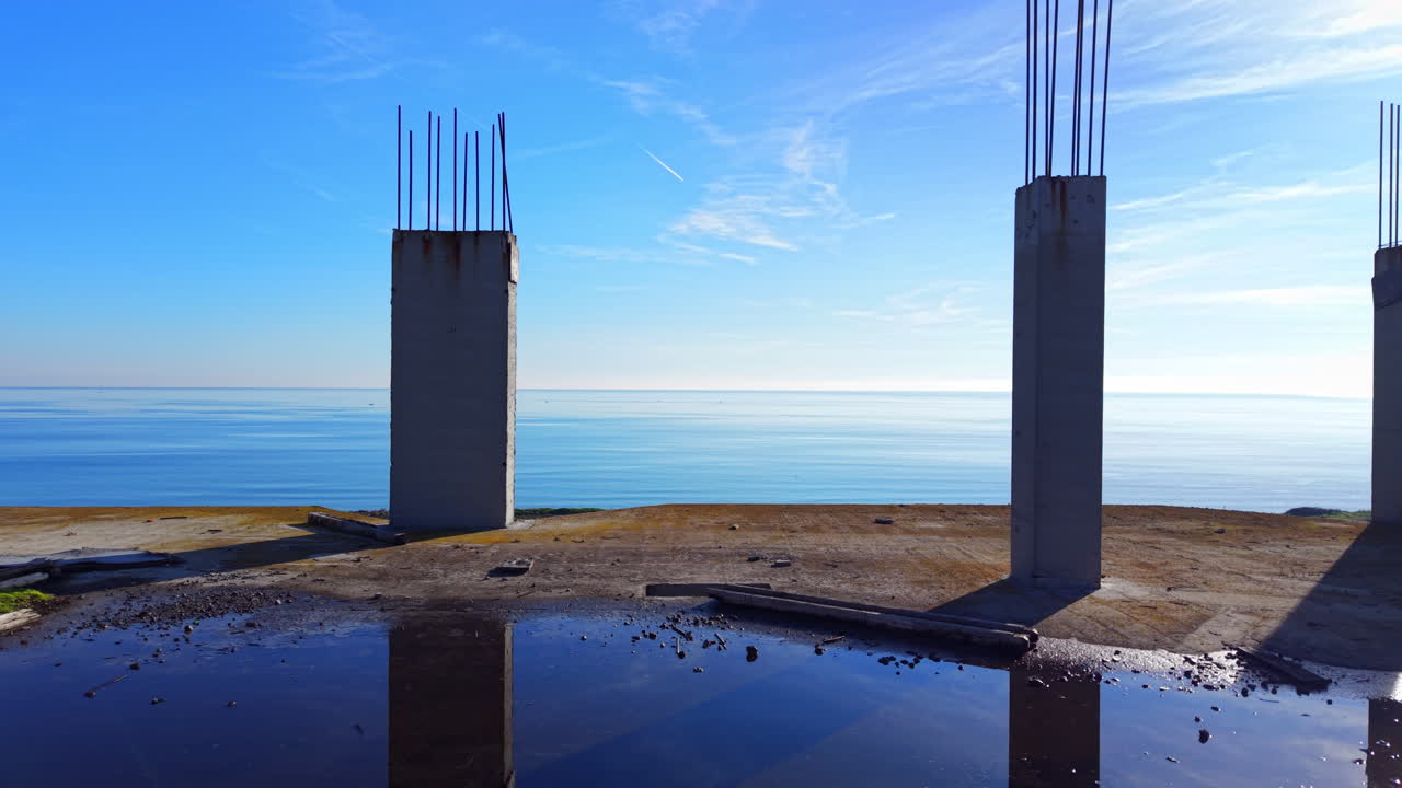 Colonne verticali in cemento armato su un cantiere che si affaccia sull'orizzonte calmo dell'oceano. Pilastri in cemento di una struttura incompiuta contro il mare blu. Vista aerea.