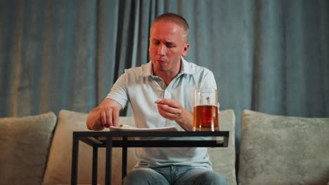 middle aged man seated in classic bar setting carefully removing bone from barbecue meat while eating, focused on task, glass of red beverage on table