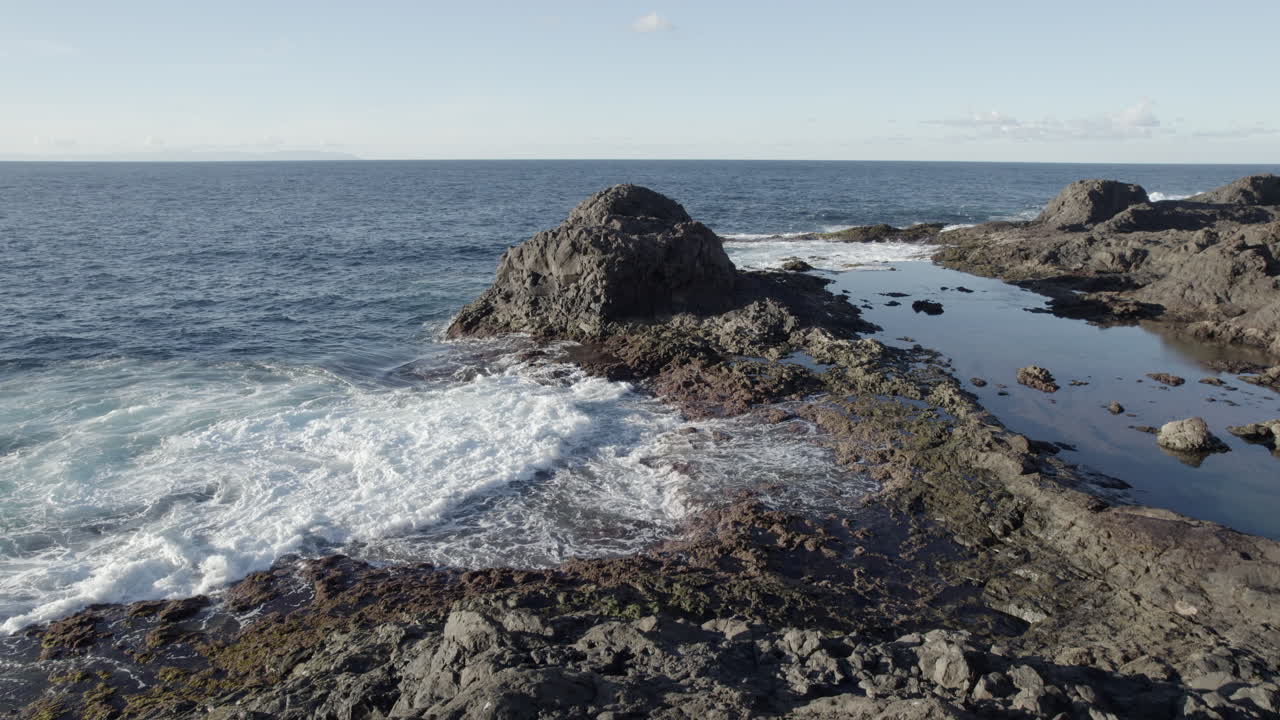 toma aerea en reversa sobre la costa de galdar y donde se puede ver a una mujer sentada en una gran roca y admirando las olas del mar y el paisaje