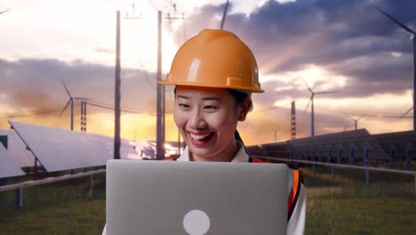 Close Up Of Asian Female Engineer With Safety Helmet Working On A Laptop With Solar Panel and Wind Turbines