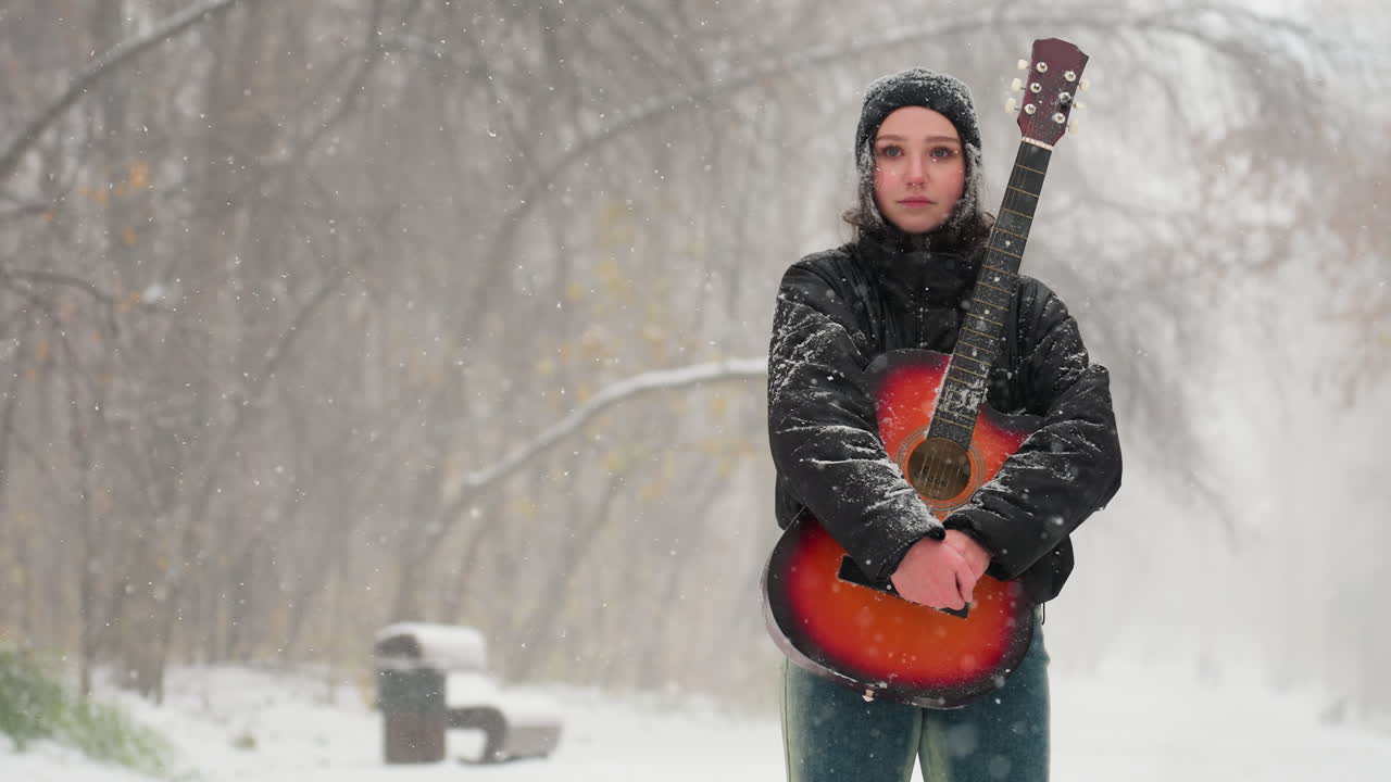 joven de pie en un parque nevado sosteniendo una vibrante guitarra acústica roja, rodeada de árboles helados y nieve que cae suavemente, capturando un momento de invierno pacífico y sereno lleno de música