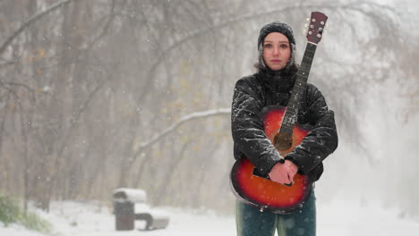 young girl standing in snowy park holding vibrant red acoustic guitar, surrounded by frosty trees and softly falling snow, capturing a peaceful and serene winter moment filled with music