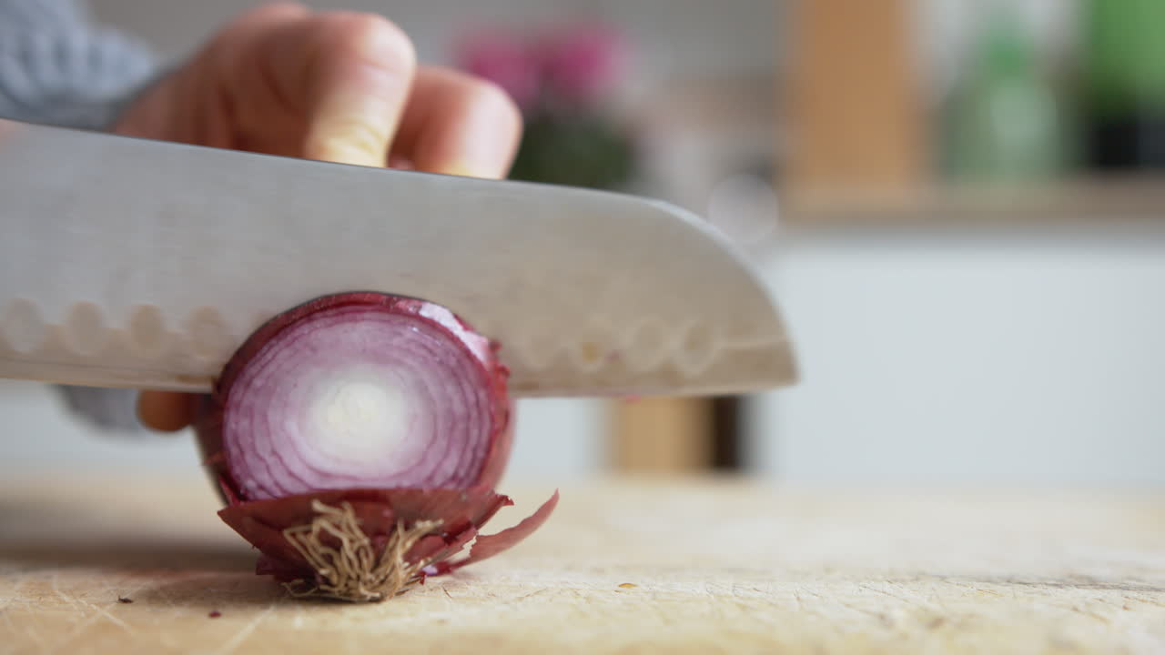 Close up woman's hand start slicing Italian red onions with a rounded sharp knife in the kitchen