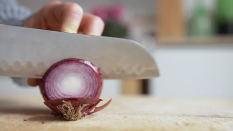 Close-up-woman's-hand-start-slicing-Italian-red-onions-with-a-rounded-sharp-knife-in-the-kitchen