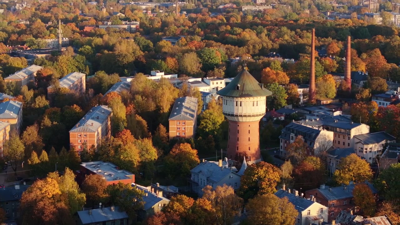 Vista aérea da Torre de Água Alīse em Riga ao nascer do sol, emoldurada por árvores de outono, 4K.