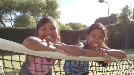 smiling girls leaning on tennis net, enjoying outdoor activity together