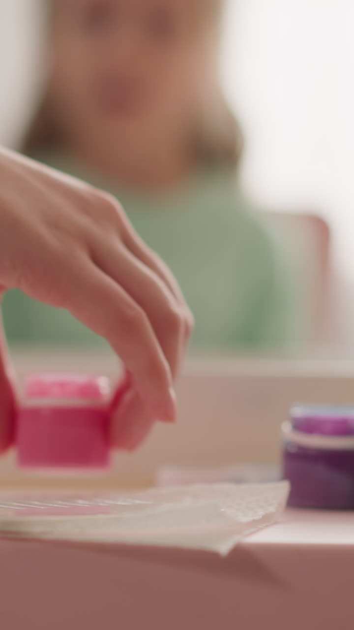 Teacher takes bottle with pink paint while little girl sits at table in classroom slow motion. Preparation for Ebru drawing lesson. Supplies for artistic work