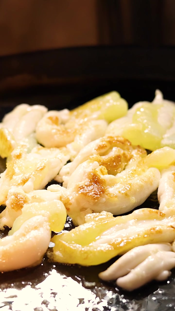Calamari e uova che friggono su piastra, pinze che girano il cibo, illuminazione calda, messa a fuoco ridotta.