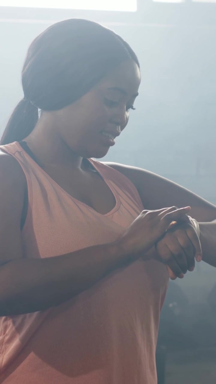 Vertical video: Timer starting, woman in pink tank and leggings tapping watch and fixing top at gym