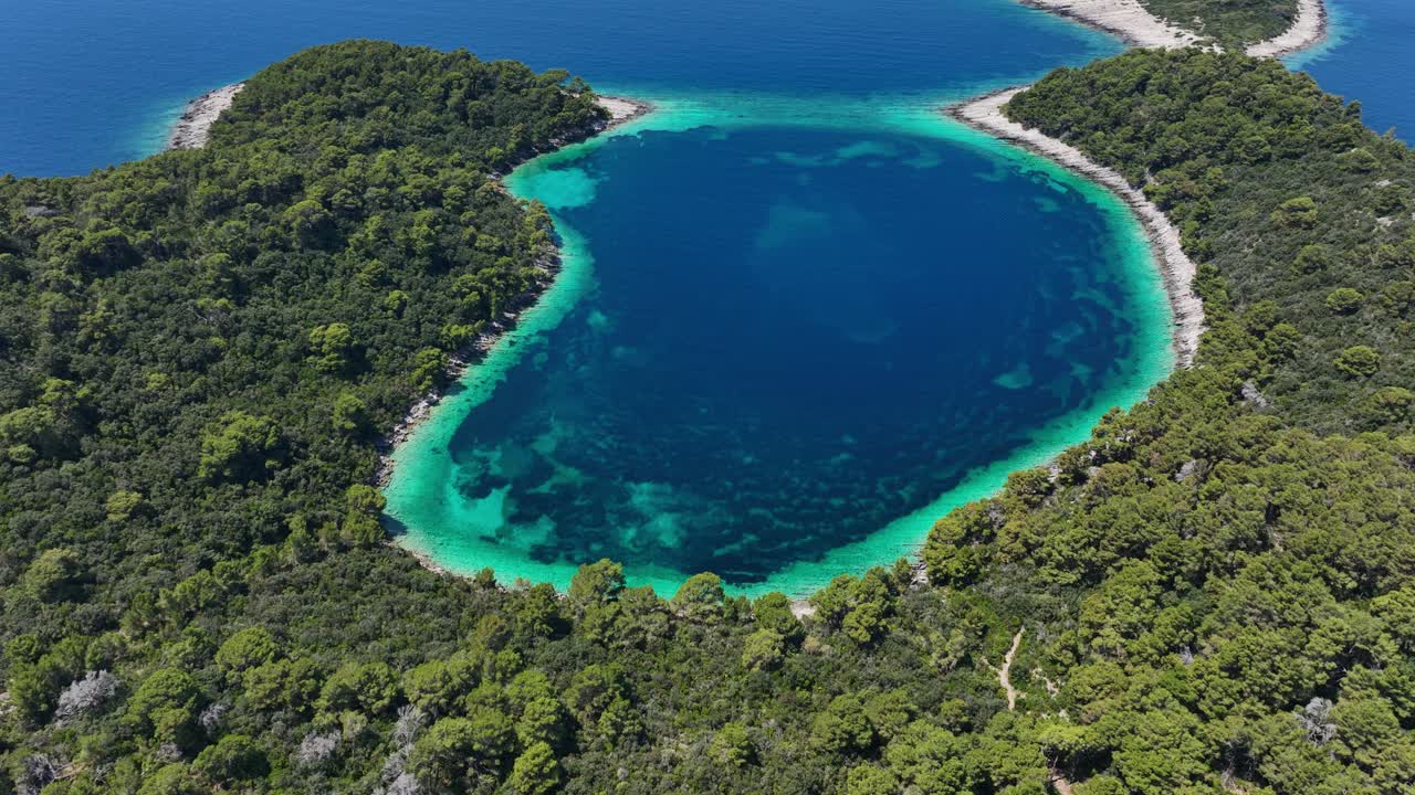 Orbit aerial view of vivid turquoise cove enclosed by forest on Mljet Island, Croatia