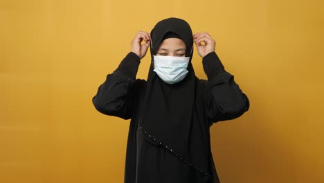 asian muslim woman wearing hijab and facial mask, against yellow background