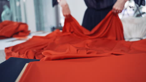 young seamstress is putting bright red fabric on the wooden table. large piece of red material in the hands of a dressmaker in workshop.