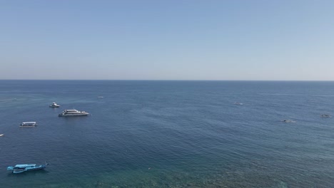 Aerial-tilts-to-distant-blue-sky-horizon-over-calm,-flat-ocean-on-Bali