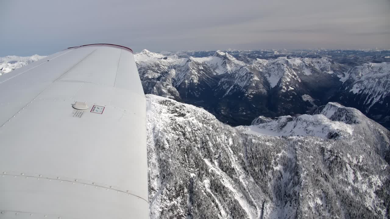 vista de la punta del ala de un avión ligero volando sobre un paisaje montañoso nevado