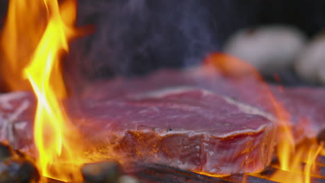 close up of flame grilling raw sirloin beef steak on hot bbq with smoke in slow motion 4k