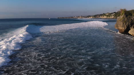 Volando-Sobre-El-Hermoso-Océano-Azul-Con-Enormes-Olas-Golpeando-La-Costa-En-Un-Famoso-Lugar-De-Surf-En-Uluwatu,-Bali