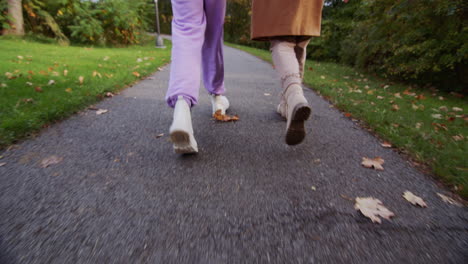 rear view: two women walk along the path in the autumn park, walk side by side, only the legs are visible in the frame.