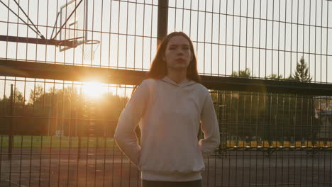 joven de pie en una cancha de baloncesto al atardecer