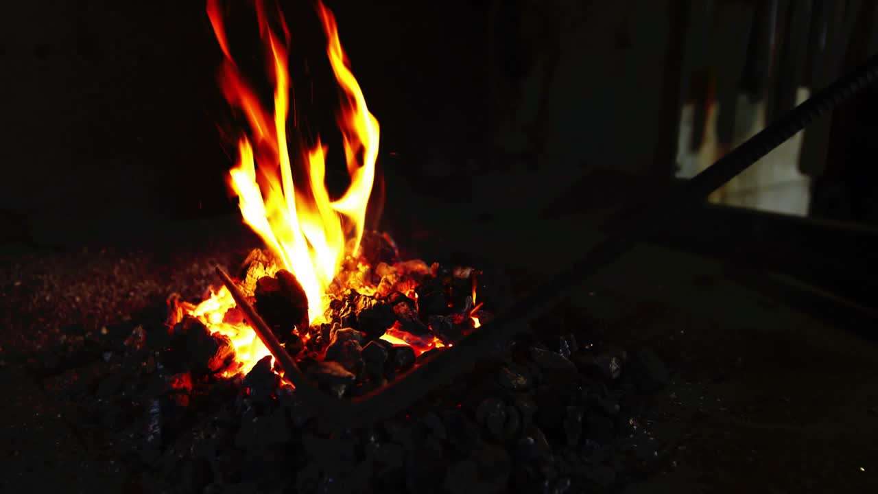 Glowing charcoal pieces igniting flames, metal rod plunging into fire to heat tip, embers drifting