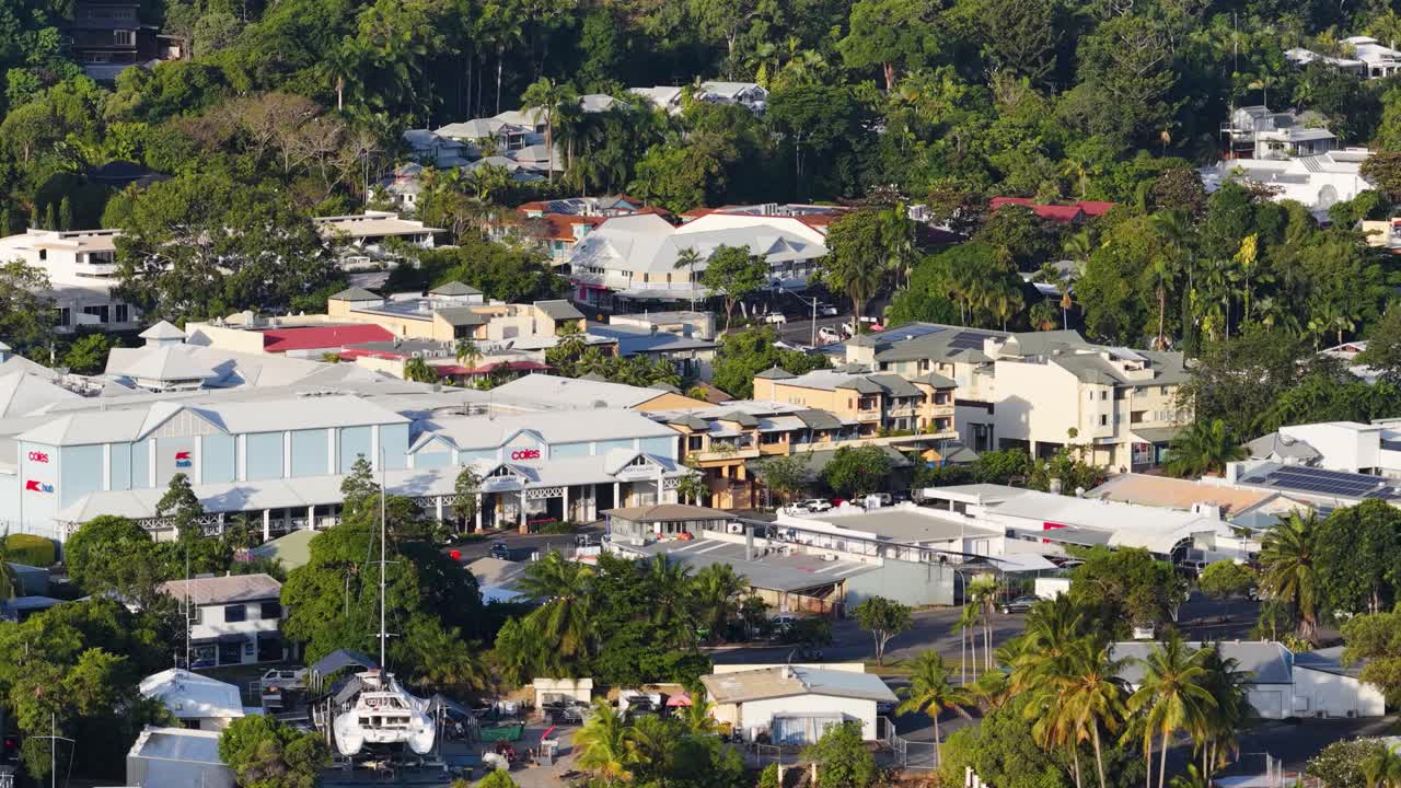 Drone footage captures Port Douglas' vibrant town, showcasing shops, houses, and lush greenery under bright daylight