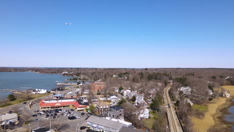 el avión vuela a través de un cielo azul y claro sin nubes sobre un pequeño pueblo al lado de un lago con estación de tren