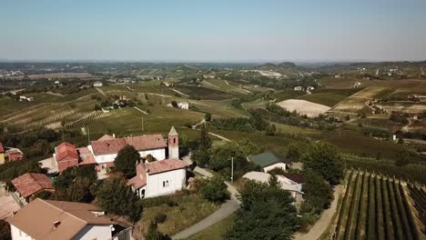 aerial view, slow push in small village with old church and bell tower in the hills of piedmont