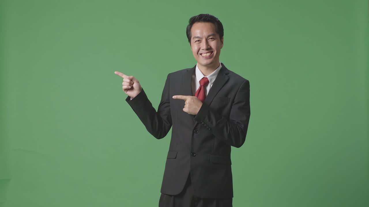 An Asian Business Man With A Smile Pointing To The Side While Standing In The Green Screen