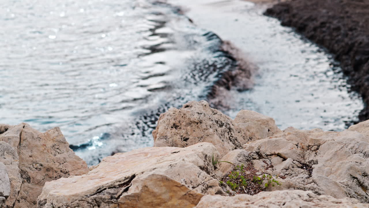 Primo piano di rocce bianche e frastagliate con onde scure che si infrangono su una riva fangosa sullo sfondo